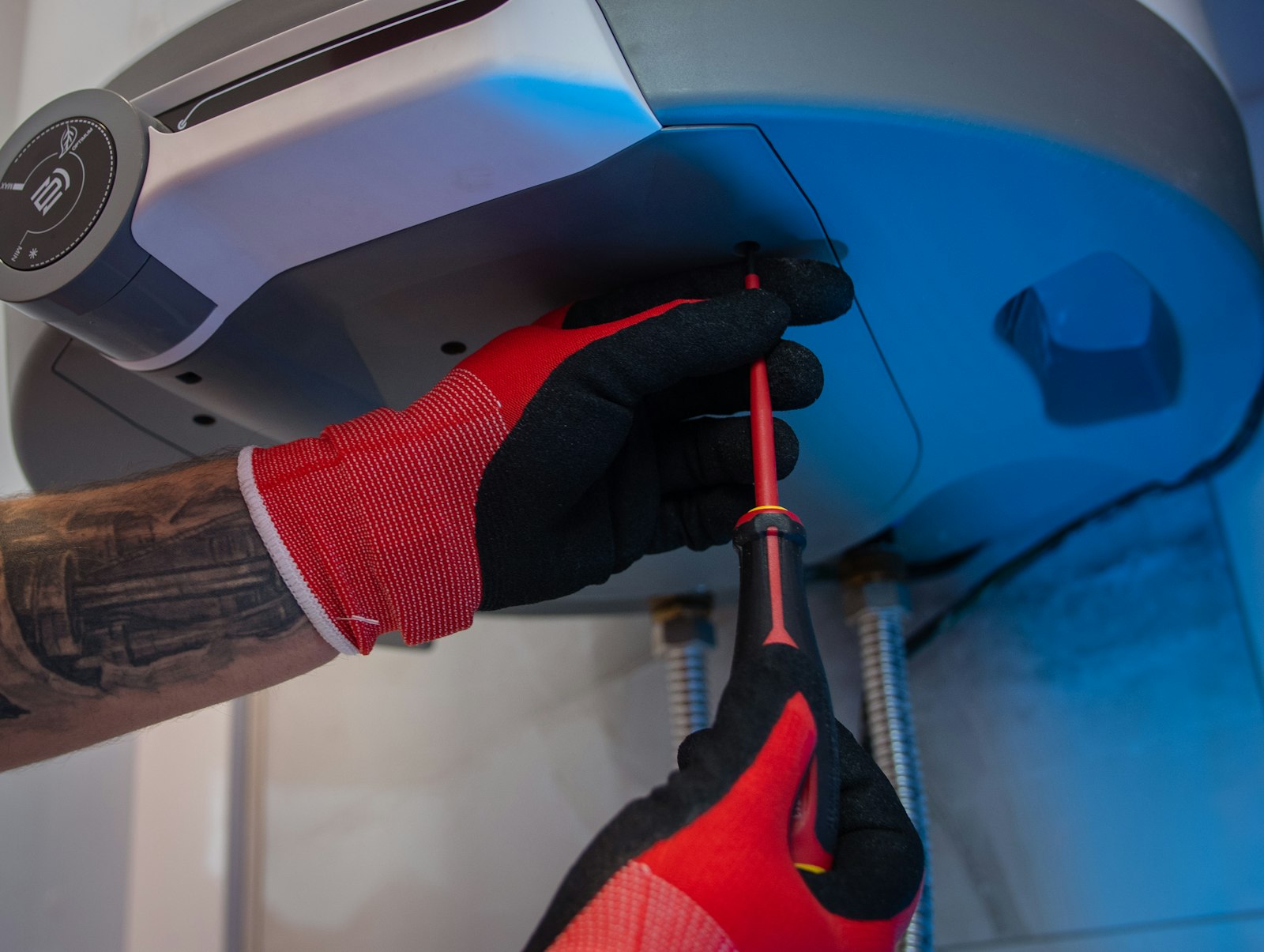 Appliance technician's gloved hands opening a unit's service panel with a screwdriver