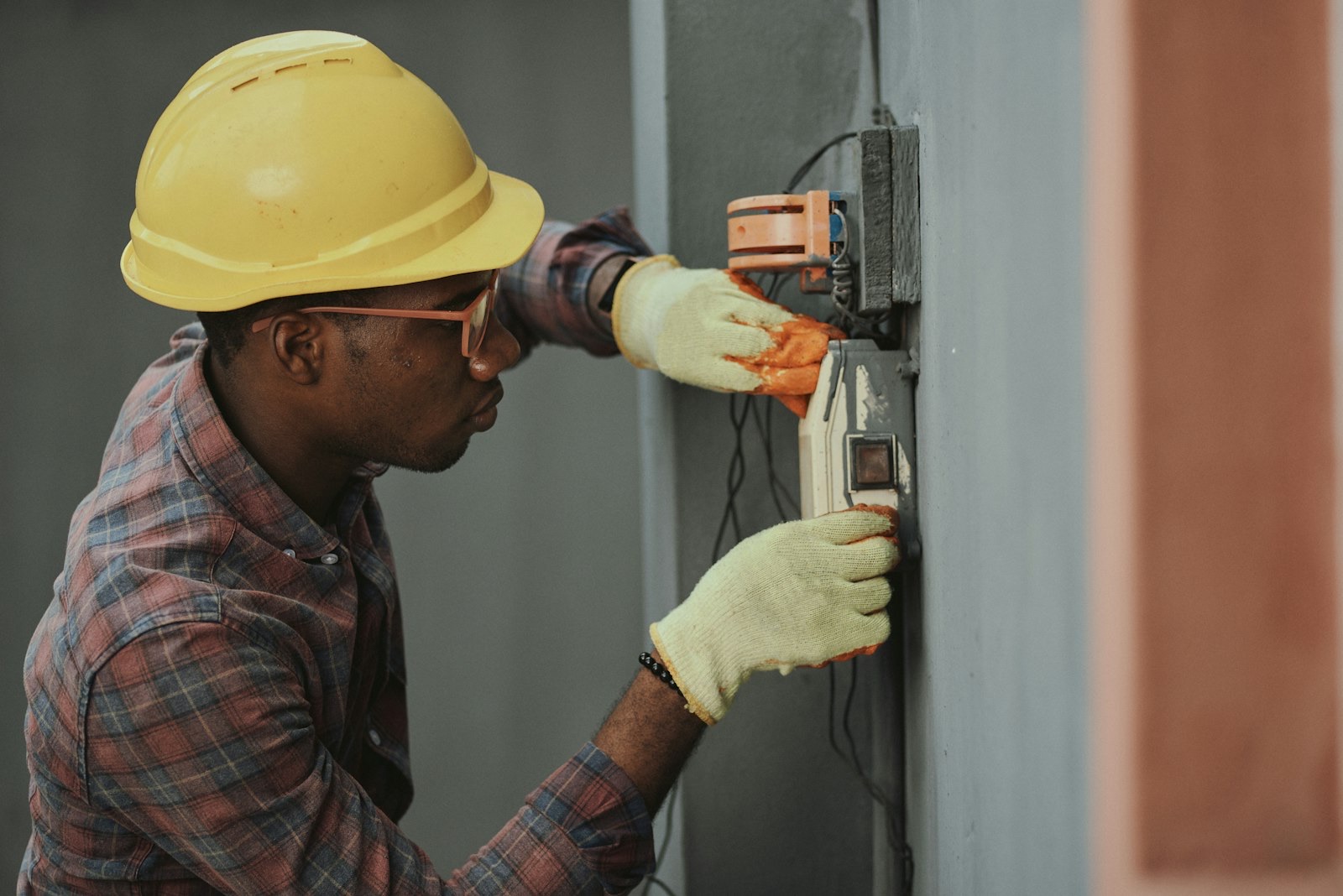 Electrician in a hard hat wiring a meter box on a wall