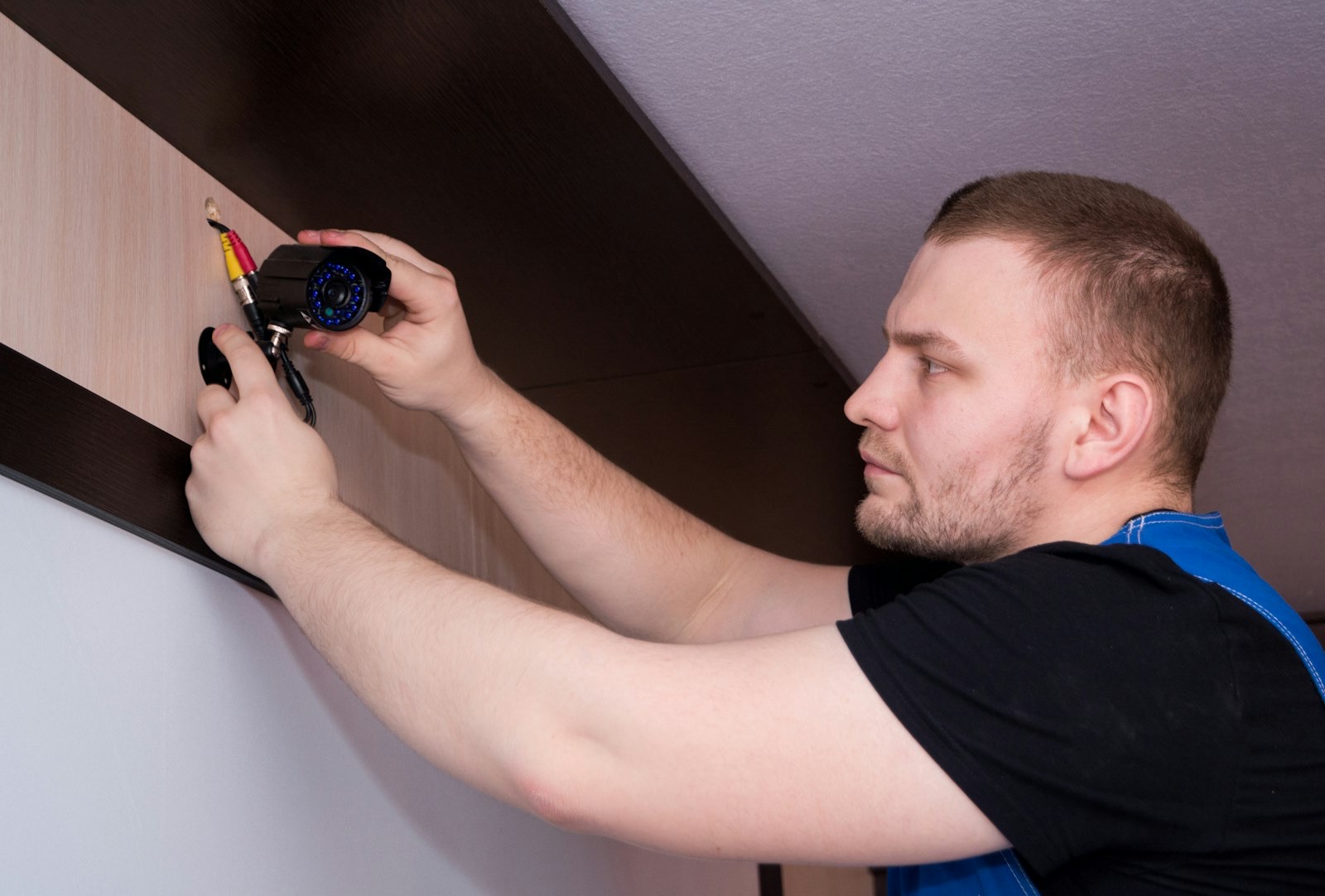Handyman mounting and wiring a small security camera on an interior wall