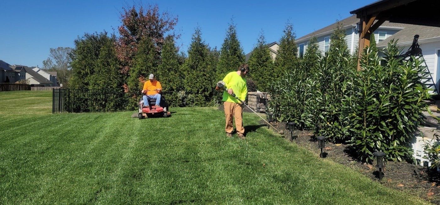 Landscaping crew mowing and edging a residential lawn on a sunny day