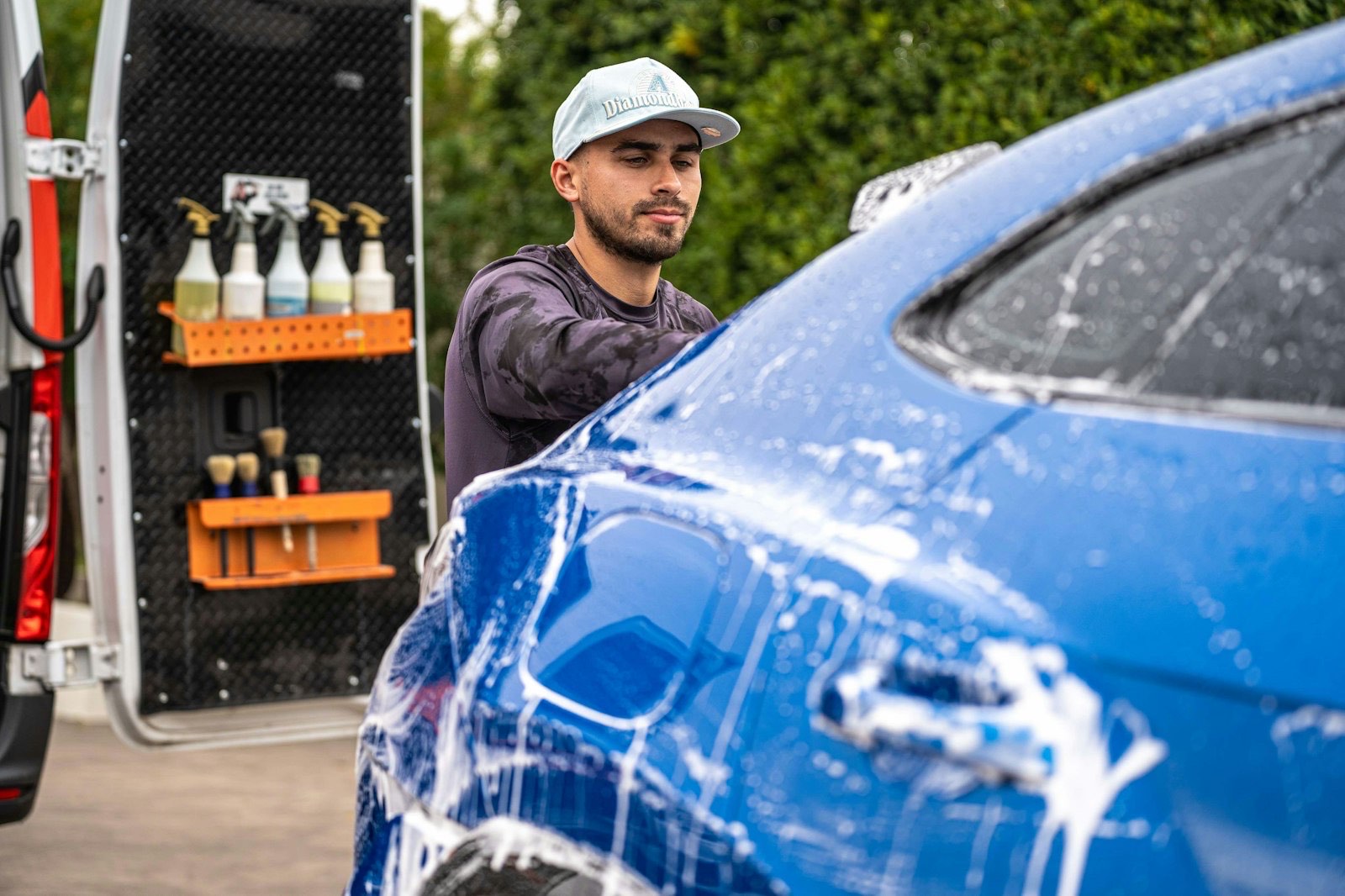 Mobile detailer washing a soaped-up car beside his fully equipped service van