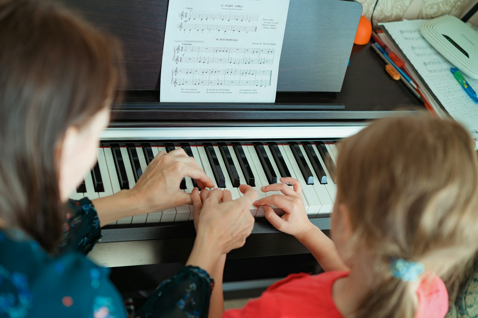 Piano teacher guiding a young student's hands across the keys during a lesson