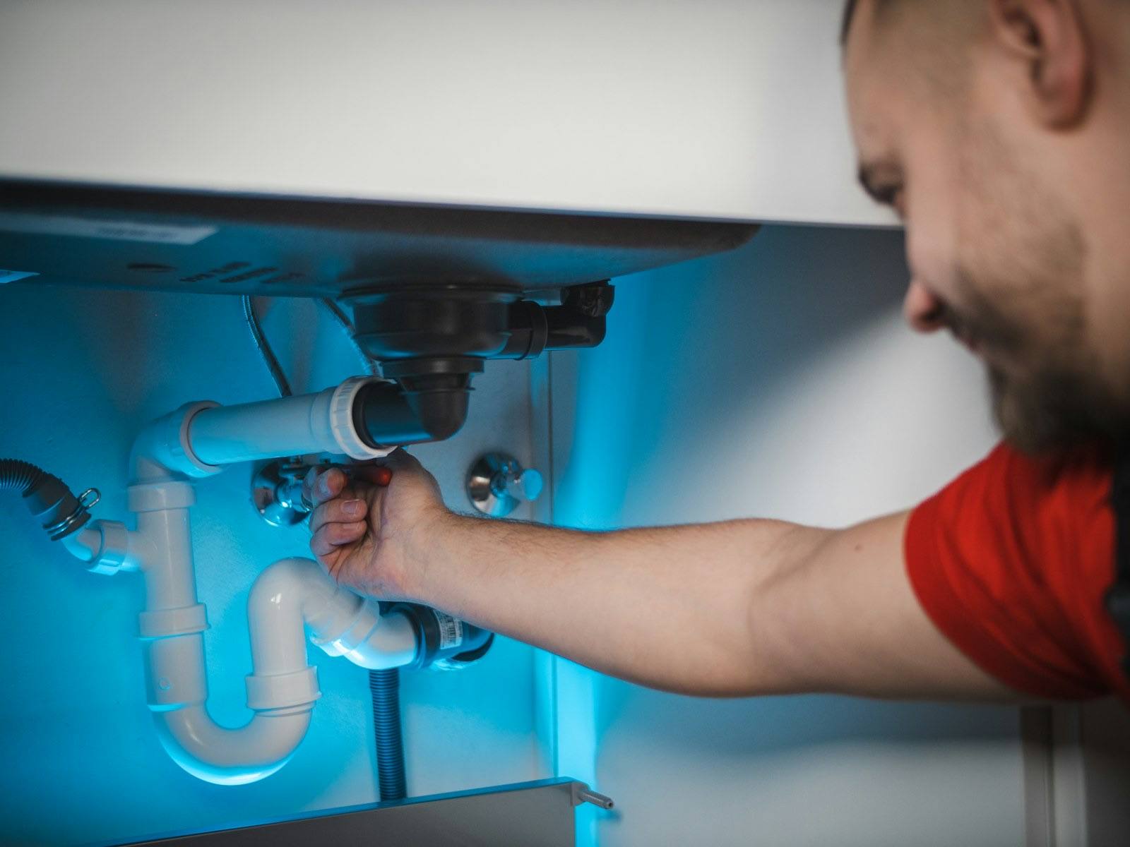 Plumber tightening the drain trap under a kitchen sink