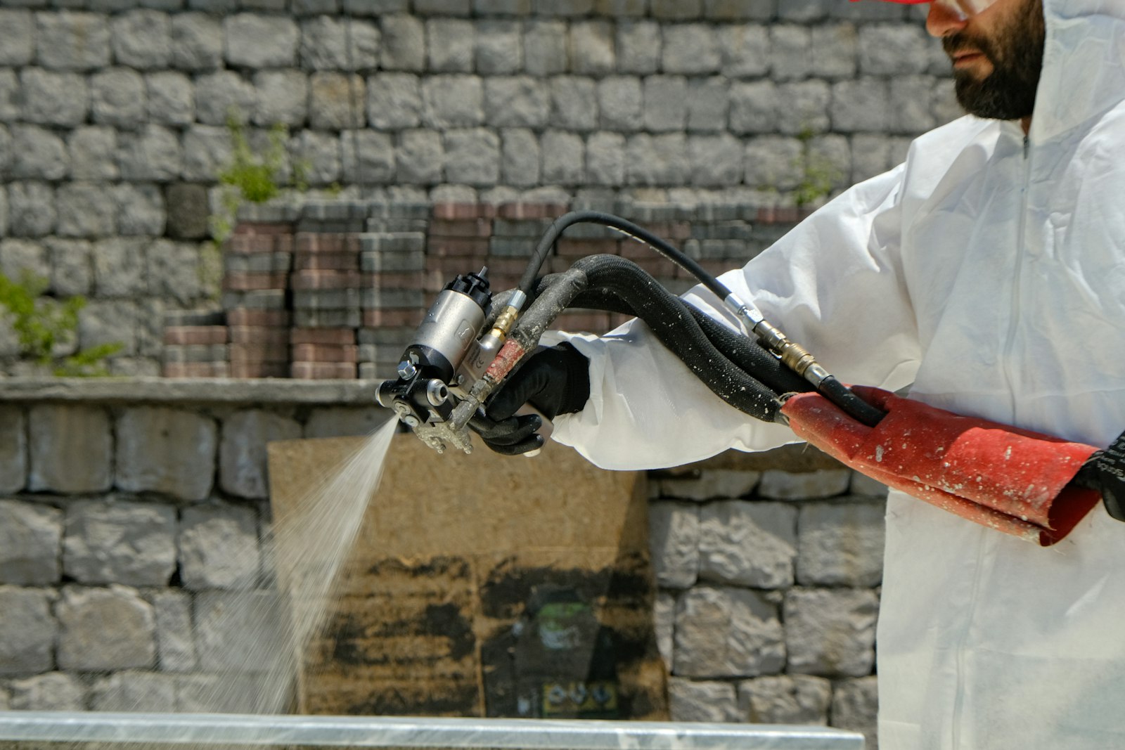 Restoration technician in protective coveralls applying a spray treatment with a rig