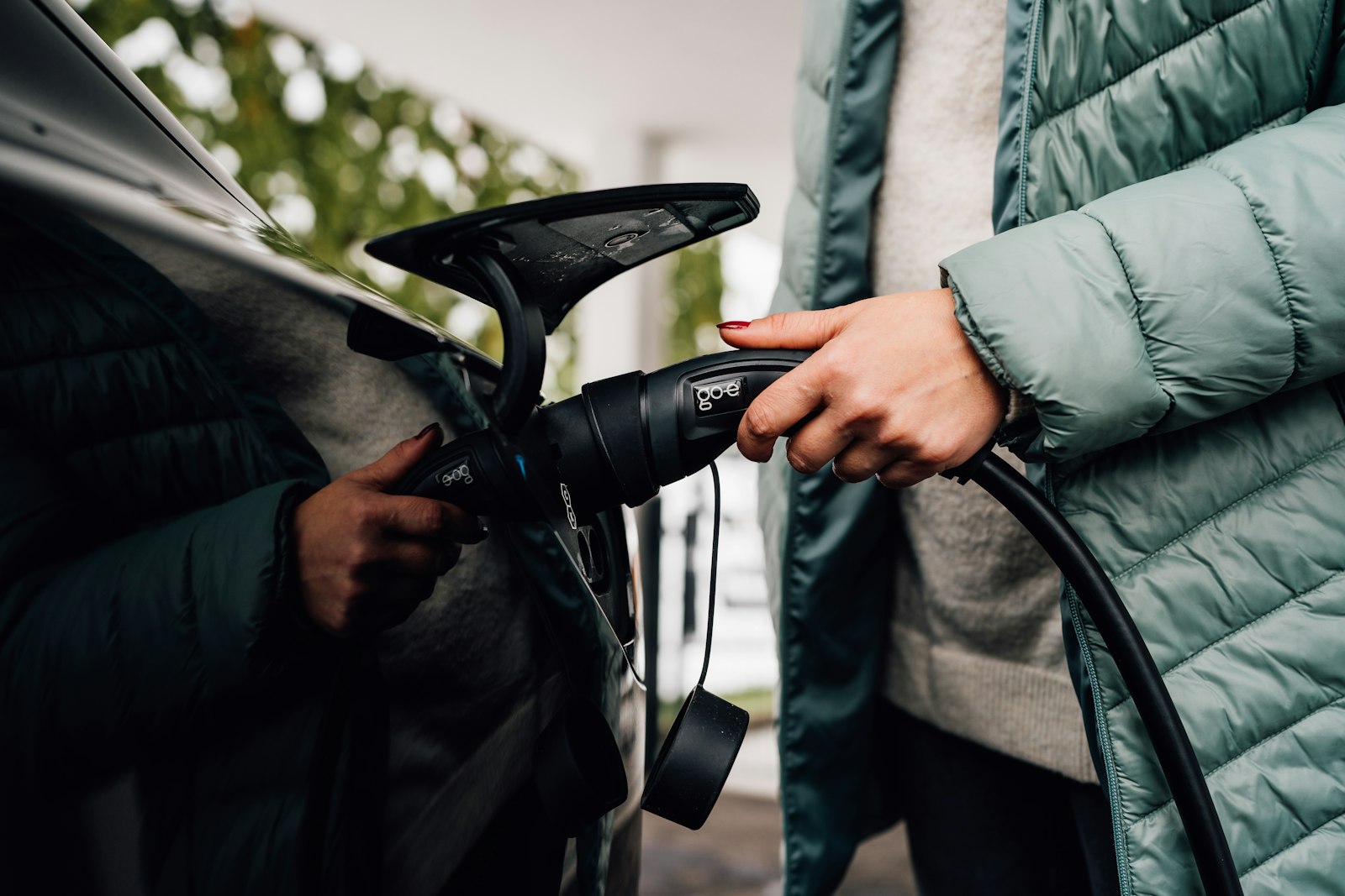 Homeowner's hands plugging an EV charging cable into a car at home