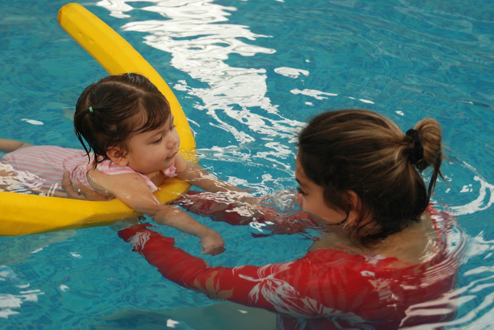 Swim instructor in the water supporting a toddler floating on a swim noodle