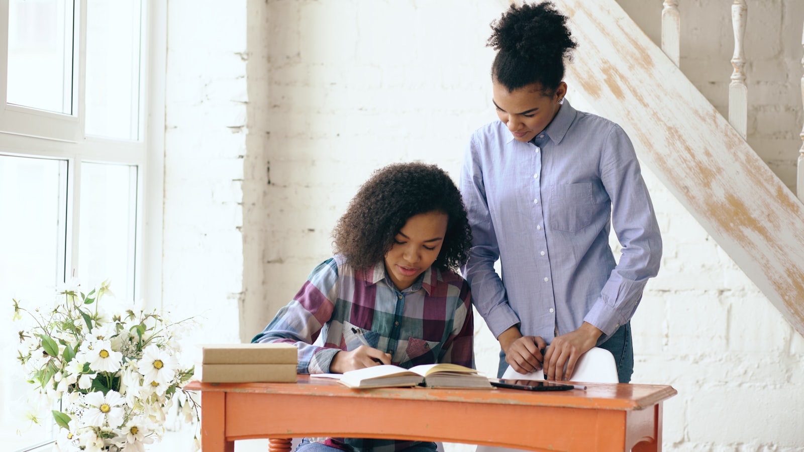 Tutor leaning over the table to help a student work through her notebook